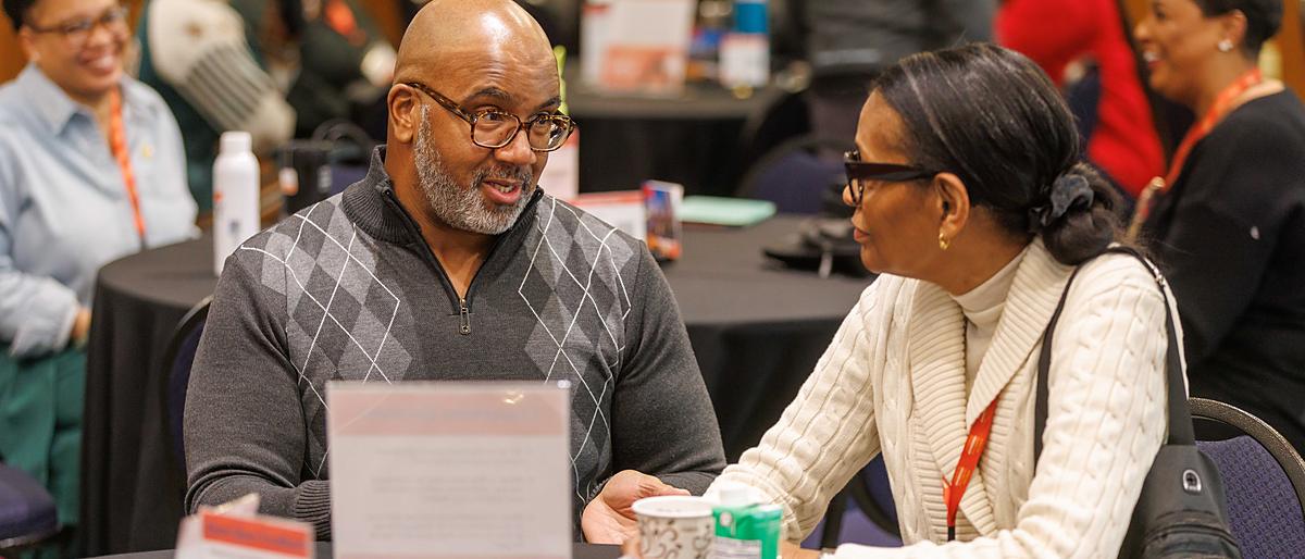 Two attendees in close conversation across a table between sessions.
