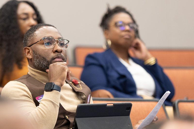 An attendee rests his chin on his hand, tablet and notes in front of him, listening closely during a session.
