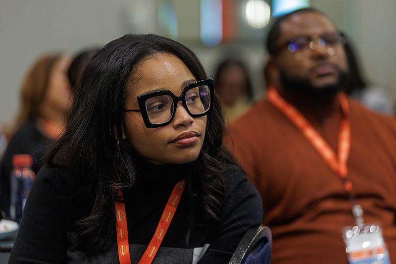 An attendee listens closely during a session, with other participants seated nearby.