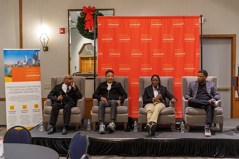 Four panelists seated on stage in front of an African American Leadership Academy backdrop.
